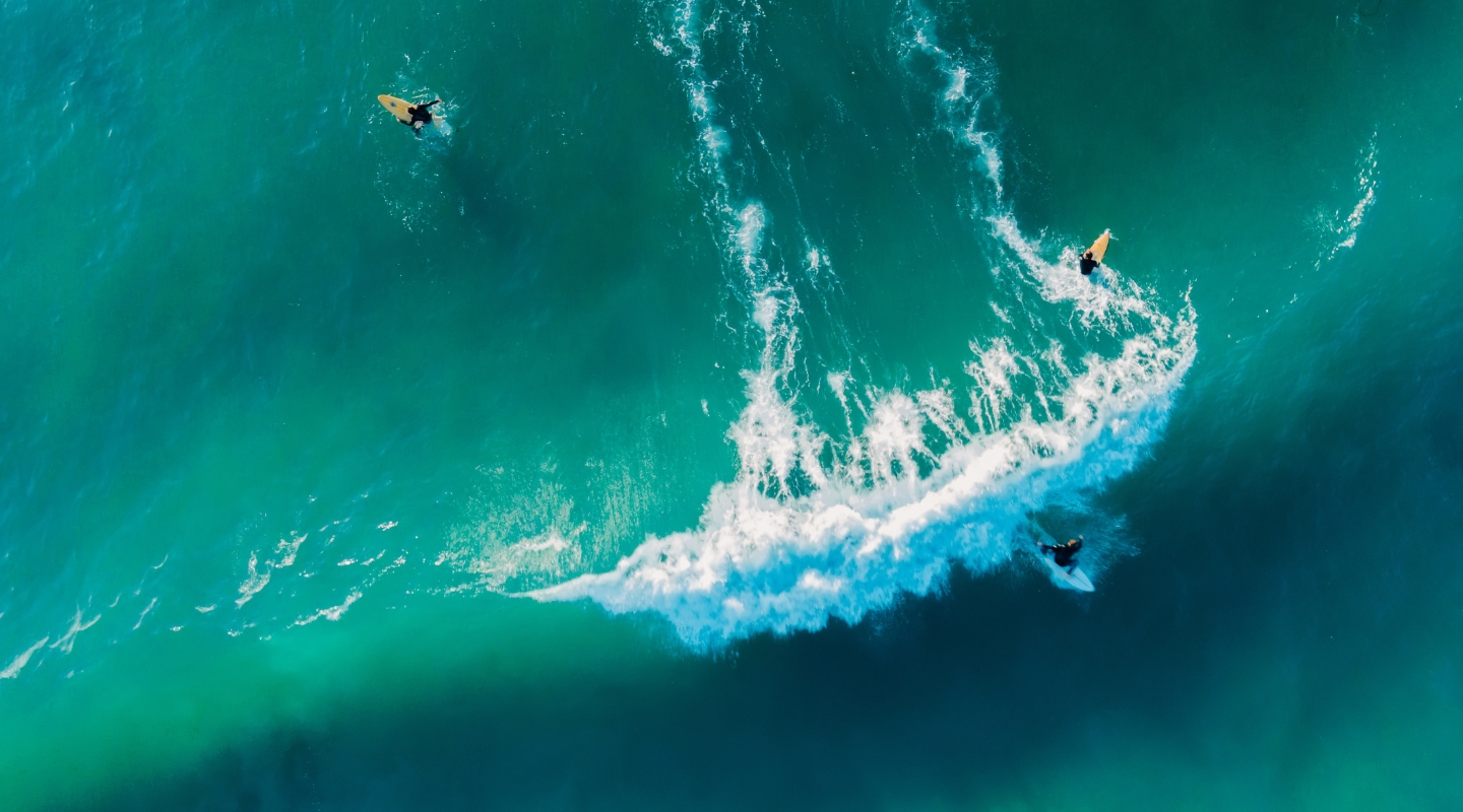 Surfers riding a wave from above representing agility and control for insurance, life & protection providers - hero image